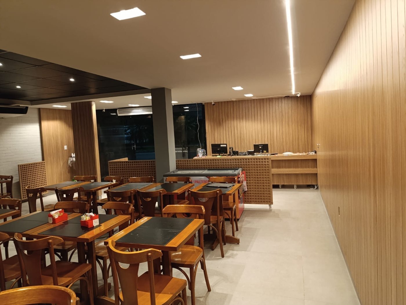 Restaurante com painel de madeira ripada, bancada e mesas